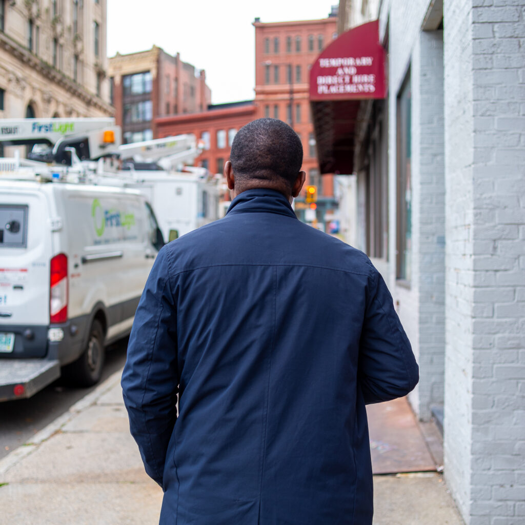 Sergio stands with his back to the camera on the sidewalk downtown.